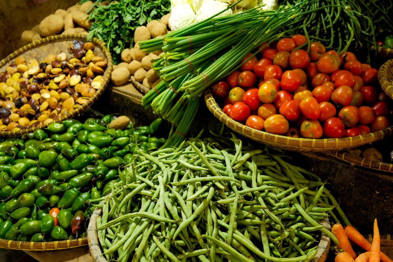 Baskets of fresh produce at a market — tomatoes, green beans, peppers, herbs.